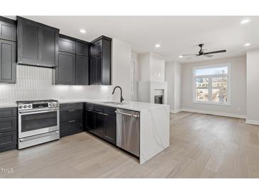 Modern kitchen with black cabinetry, stainless steel appliances, and a center island with a waterfall countertop at 226 Woodsborough Pl, Raleigh, NC 27601