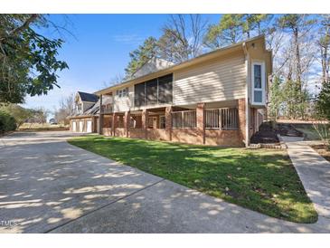 Side angle of a tan home featuring a brick foundation and a spacious driveway, surrounded by mature trees at 6301 King Lawrence Rd, Raleigh, NC 27607