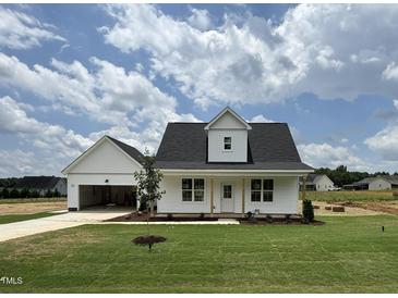 Charming exterior view of a white home with a manicured lawn and a detached garage at 432 Springtooth Dr, Zebulon, NC 27597