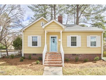 Charming yellow home featuring a brick foundation, blue door, white shutters and a landscaped front yard at 2618 Elgin St, Durham, NC 27704