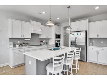 Bright kitchen features white cabinets, stainless steel appliances and island with bar stool seating at 90 Rigsby Ave, Four Oaks, NC 27524