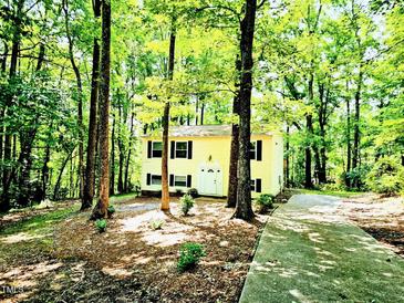 Charming yellow two-story home surrounded by lush trees and greenery, providing a serene and private setting at 325 Bainbridge Cir, Garner, NC 27529