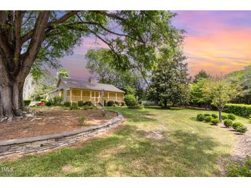 Charming home with covered porch, stone wall feature, and mature trees in a spacious front yard at 8324 Humie Olive Rd, Apex, NC 27502