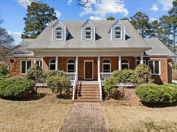 Charming brick home featuring a welcoming front porch, dormer windows, and professionally landscaped yard at 6336 Wrenwood Ave, Raleigh, NC 27607