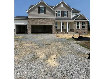 New two-story home featuring stone accents, a covered front porch, and an attached three-car garage at 72 Cultivator Ct, Angier, NC 27501