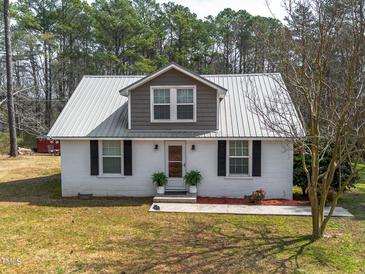 Charming home featuring a metal roof, white brick, black shutters, and tasteful landscaping at 3130 State Hwy 58, Louisburg, NC 27549