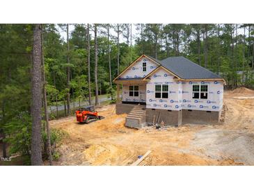 New construction home with brick foundation, black roof, and protective wrap against wooded backdrop at 15 Bourbon St, Fuquay Varina, NC 27526