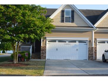 Inviting townhouse featuring a two-car garage, manicured lawn, and stone accents at 63 Radcliffe Ct, Clayton, NC 27527