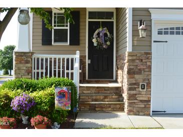 Charming home entrance with stone accents, a wreath, and potted plants for inviting curb appeal at 63 Radcliffe Ct, Clayton, NC 27527