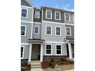 View of townhomes featuring neutral color palettes, stone accents, and ample windows under a partly cloudy sky at 3011 Honeymyrtle Ln, Durham, NC 27703