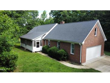 Classic brick home featuring an attached garage, screened porch, and manicured lawn surrounded by mature trees at 3560 Nc 98, Youngsville, NC 27596