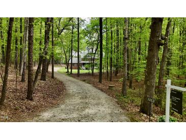 Secluded two-story brick home nestled among trees with a long gravel driveway and for sale sign at 1013 Traders Trl, Wake Forest, NC 27587