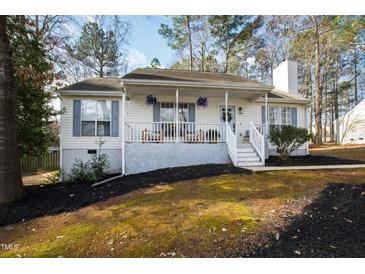 Charming home featuring a cozy front porch with lovely hanging floral arrangements and manicured landscaping at 224 Round About Rd, Holly Springs, NC 27540