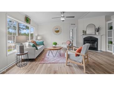Cozy living room featuring a fireplace, wood floors, and abundant natural light from a large window at 92 Papoose Trl, Lillington, NC 27546