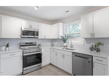 Bright kitchen features stainless steel appliances, white cabinets, and light backsplash at 1206 Dubose St, Garner, NC 27529