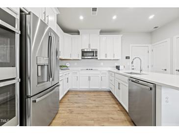 Bright kitchen featuring stainless steel appliances, white cabinetry, and a large island with quartz countertops at 600 Hedrick Ridge Road # 108, Cary, NC 27519