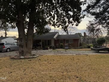 Cozy brick home features a covered porch, a gravel driveway and a mature shade tree in the front yard at 902 Bragg St, Sanford, NC 27330