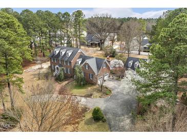 Stunning aerial view of a brick home featuring a circular driveway and well-manicured lawn surrounded by mature trees at 3715 Rawls Church Rd, Fuquay Varina, NC 27526