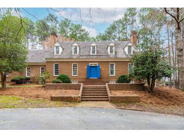 Stately brick home with a blue door and brick steps leading to the entrance, set amongst mature trees at 10726 Trego Trl, Raleigh, NC 27614