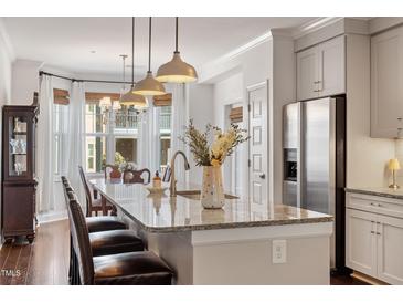 Bright kitchen with stainless steel refrigerator, granite countertop island, and elegant lighting fixtures at 714 Waterford Lake Dr, Cary, NC 27519