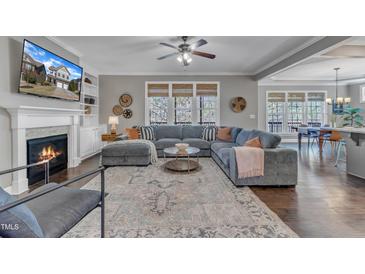Bright living room features a fireplace, large windows, ceiling fan, and spacious seating area with grey sectional sofa at 205 Virginia Water Dr, Rolesville, NC 27571