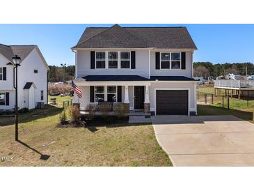 Charming two-story home featuring gray siding, a one-car garage, and a welcoming front porch with an American flag at 38 Winter Red Way, Benson, NC 27504