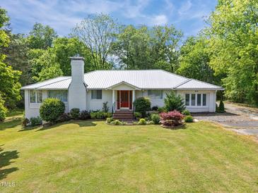 Charming single-story home with a white exterior, red front door, lush lawn, and mature landscaping at 513 N Nash St, Hillsborough, NC 27278