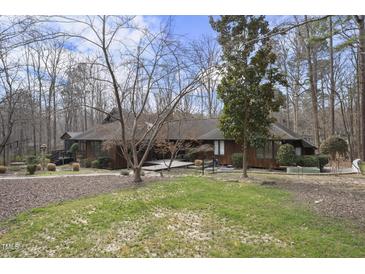 A sprawling single-story home with wooden facade surrounded by a lush wooded landscape and front yard at 10509 Leslie Dr, Raleigh, NC 27615