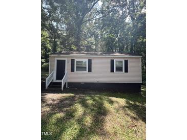 Charming one-story home featuring black shutters, a black door, and light siding nestled among mature trees at 158 Torain St, Hillsborough, NC 27278