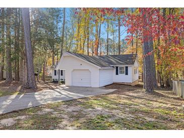 Charming single-story home with white siding, attached garage, and a driveway surrounded by colorful trees at 1001 Atchison St, Garner, NC 27529