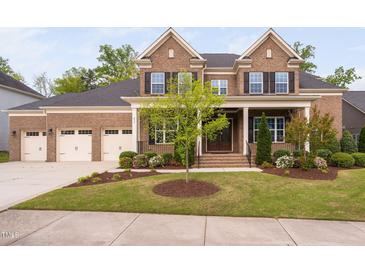 Charming brick home with a manicured lawn, three car garage, beautiful landscaping, and covered porch at 832 Mountain Vista Ln, Cary, NC 27519