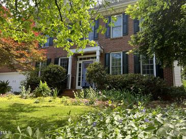 Charming two-story brick home with manicured lawn, blooming flowers, and black shutters at 307 Kellyridge Dr, Apex, NC 27502