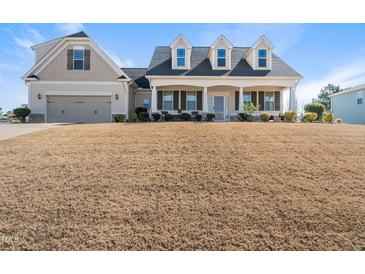 Inviting two-story home featuring dormer windows, covered porch, attached garage, and lawn on a sunny day at 21 Tracker Ct, Garner, NC 27529