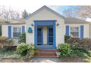 Charming home featuring a symmetrical facade with blue trim and shutters, complemented by lush, mature landscaping at 1301 Clarendon St, Durham, NC 27705