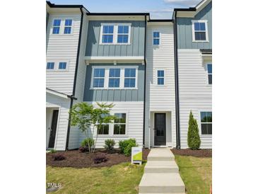 A modern, three-story townhome with a light blue and white facade, and a manicured lawn at 1028 Zelkova Ln, Chapel Hill, NC 27517