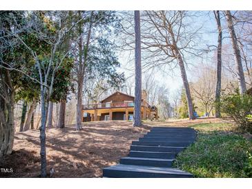 View of home with brick chimney surrounded by trees, showcasing elevated deck and long staircase entrance at 48 Blue Heron Ln, Roxboro, NC 27574