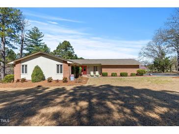 Charming single-story home with a brick facade, manicured lawn, and a bright red front door at 7516 Mourning Dove Dr, Sanford, NC 27332