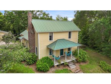Charming yellow home with a green metal roof, brick chimney, and inviting front porch with blue chairs at 2409 Hodges Rd, Burlington, NC 27217