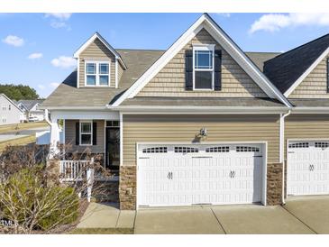 Charming exterior showcasing a two-car garage, stone accents, neutral siding, and classic architectural details under a bright blue sky at 78 Radcliffe Ct, Clayton, NC 27527