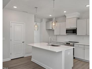Bright kitchen features an island, stainless appliances, pendant lights, and white cabinetry at 303 Old Fashioned Way, Lillington, NC 27546