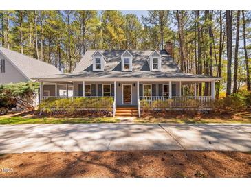 Charming Cape Cod home with a welcoming wrap-around porch surrounded by mature trees and landscaping at 7917 Blaney Franks Rd, Apex, NC 27539