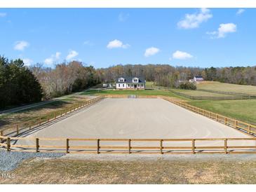 Expansive equestrian arena with wood perimeter fencing and a beautiful white farmhouse in the background on a sunny day at 2142 Henderson Tanyard Rd, Pittsboro, NC 27312