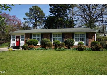 Charming brick home with a manicured front yard, trimmed shrubs and a vibrant red front door at 3516 Apache Dr, Raleigh, NC 27609