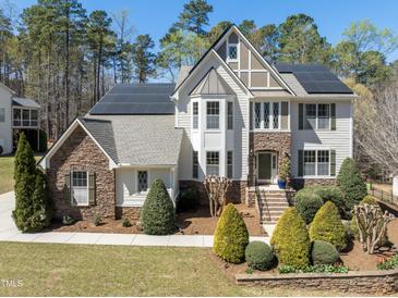 Inviting two-story home featuring stone accents, solar panels, a landscaped yard, and manicured shrubbery at 12812 Baybriar Dr, Raleigh, NC 27613