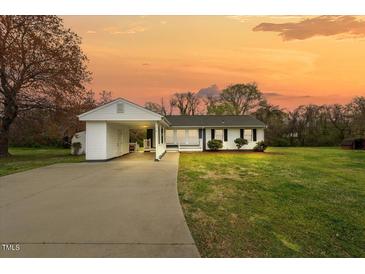 Charming single-story home featuring a connected carport, manicured lawn, and a welcoming front porch under an orange sunset sky at 118 Tysor Cir, Graham, NC 27253