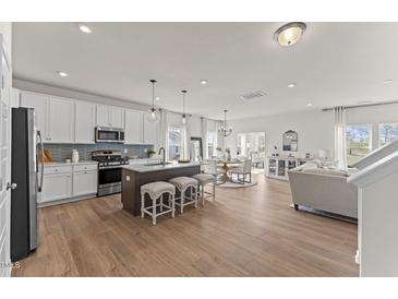 Open-concept kitchen features a center island, pendant lighting, and stainless steel appliances, blending into the dining and living spaces at 6529 Winter Spring Dr, Wake Forest, NC 27587