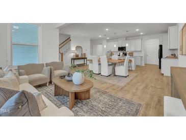 Open-concept living room with wood floors seamlessly flows into a modern kitchen and adjacent dining area at 242 Luftee Ln, Holly Springs, NC 27540