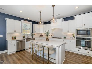 Bright, modern kitchen features white cabinets, stainless steel appliances, and a large island with seating at 332 Tumbling River Dr, Wendell, NC 27591