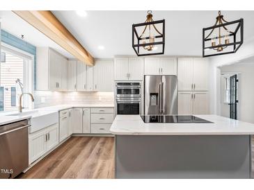 Bright kitchen featuring white cabinets, stainless appliances, island with cooktop, and modern lighting at 4012 Old Sturbridge Dr, Apex, NC 27539