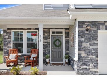 Charming front porch features stone accents, gray front door with wreath, and rocking chairs at 825 Golden Plum Ln, Zebulon, NC 27597
